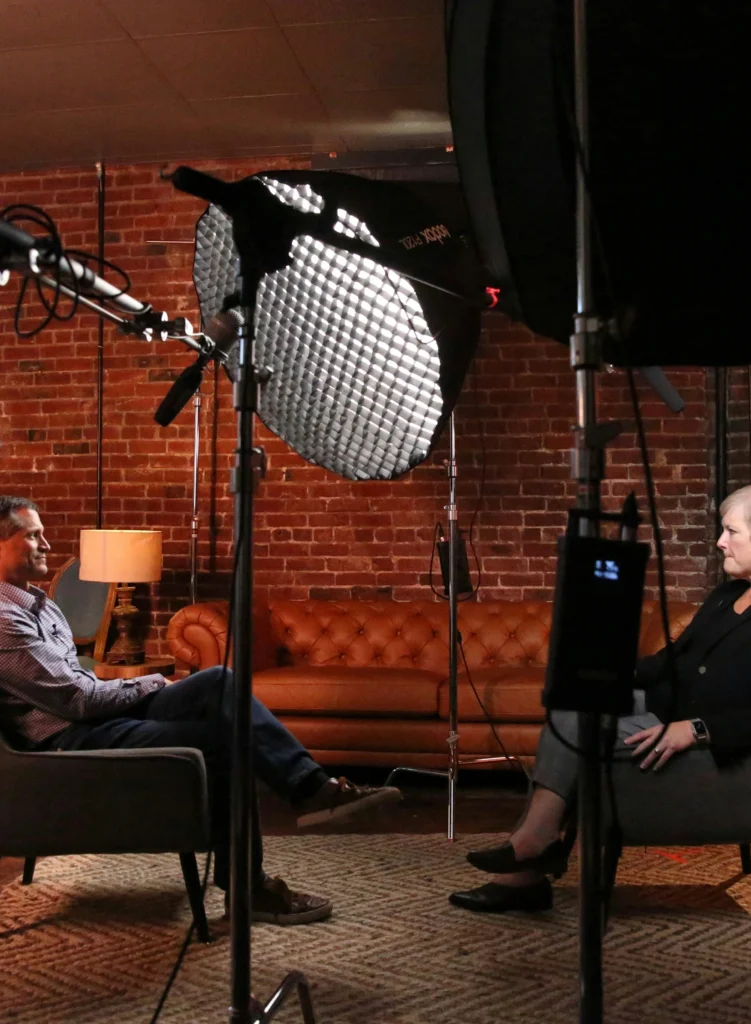 “On-camera interview being filmed with professional microphones and studio lighting.”